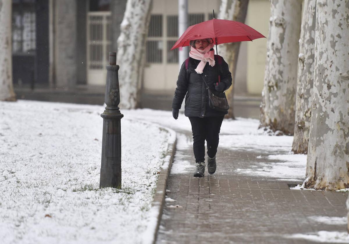 Una mujer sujeta un paraguas mientras camina por una calle de nieve.