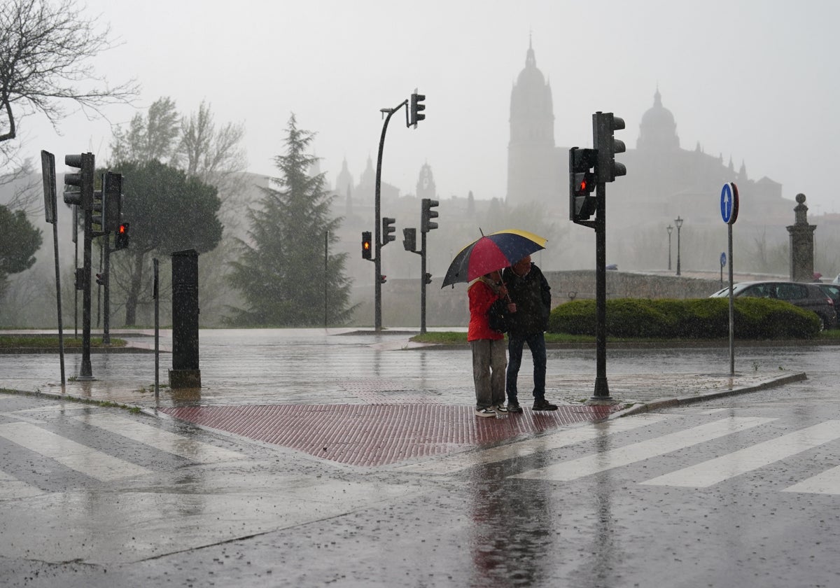 Dos personas se cobijan de la lluvia bajo un paraguas cerca del Puente Romano.