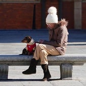 Mujer bien abrigada sentada en un banco junto a su perro.