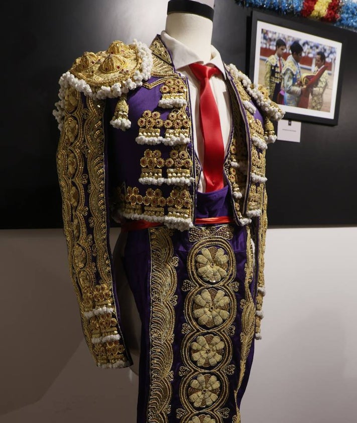 Imagen secundaria 2 - Javier Valverde junto a su familia posando con el terno donado al museo taurino, que aparece en la imagen inferior. Y en otra imagen colgando un cuadro con la fotografía de su alternativa.
