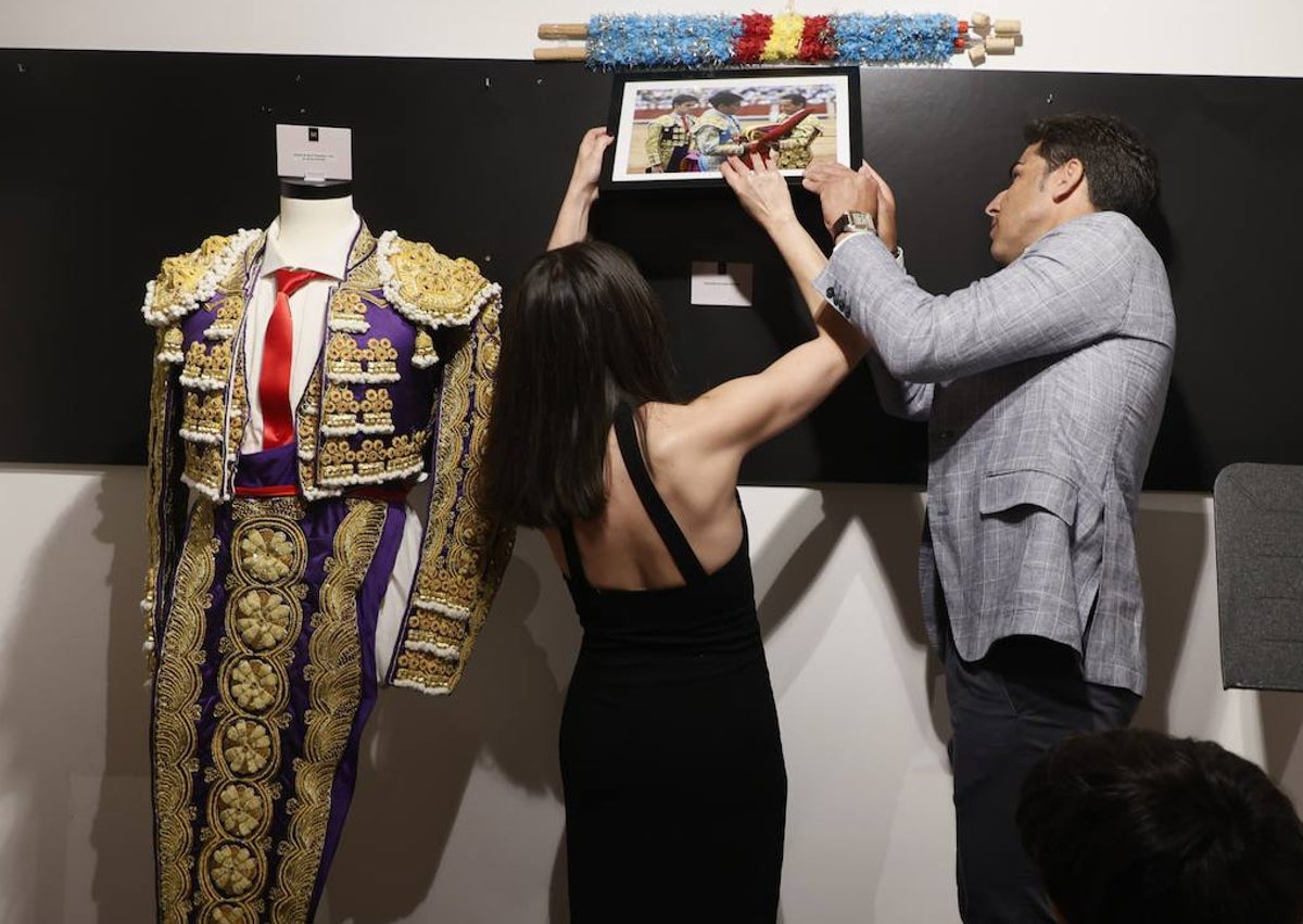 Imagen secundaria 1 - Javier Valverde junto a su familia posando con el terno donado al museo taurino, que aparece en la imagen inferior. Y en otra imagen colgando un cuadro con la fotografía de su alternativa.