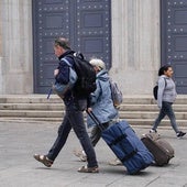 Dos personas caminan con sus maletas por la plaza de los Bandos.