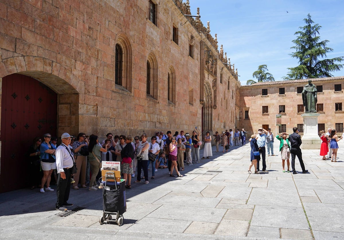 Decenas de turistas contemplan la fachada de la Universidad desde la sombra.