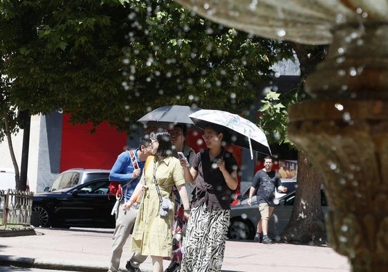 Dos personas pasean por el centro de Salamanca con dos paraguas para protegerse del calor.