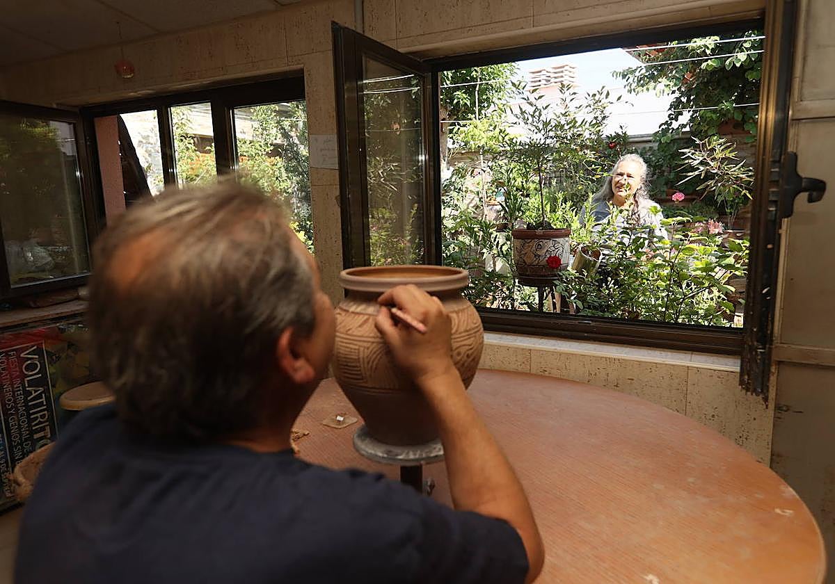 Gerardo, trabajando en una pieza en su taller mientras Reyes riega las plantas del jardín.