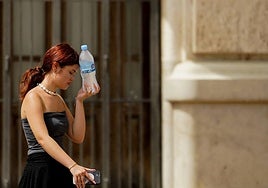 Una joven combate el calor poniéndose una botella de agua fría en la frente.