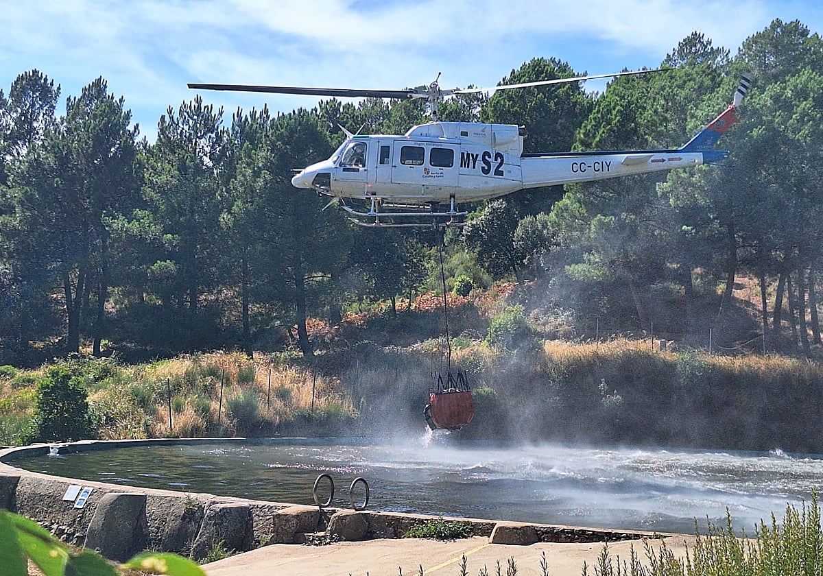 Un helicóptero carga agua en el estanque 'La Palla' para controlar el incendio en Garcibuey.