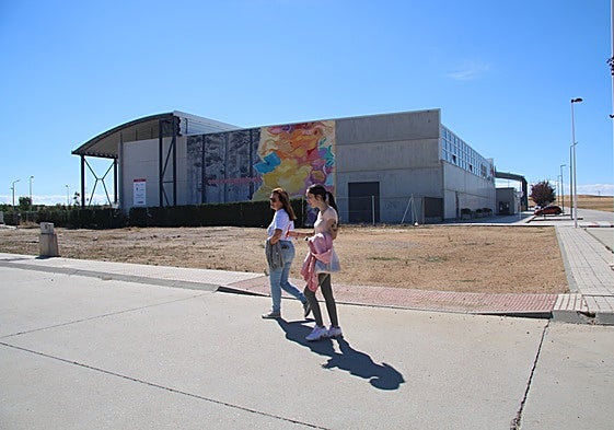 Dos mujeres pasan ante las parcelas municipales de Castellanos de Moriscos en las que se construirán las 5 viviendas protegidas de la Junta.