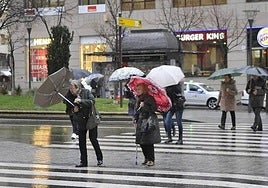 Viandantes caminando en un día de mucho viento en la capital.