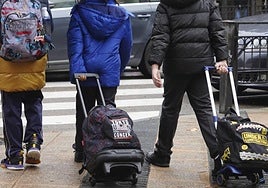 Tres escolares con sus mochilas por el centro.