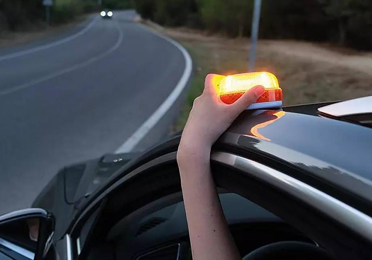 Una persona, colocando una baliza V-16 en su vehículo.