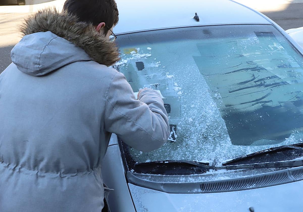 Un joven rasca un coche helado.