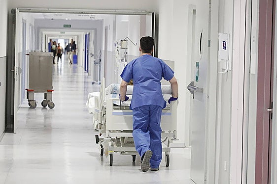 Un celador, trasladando en camilla a un paciente.