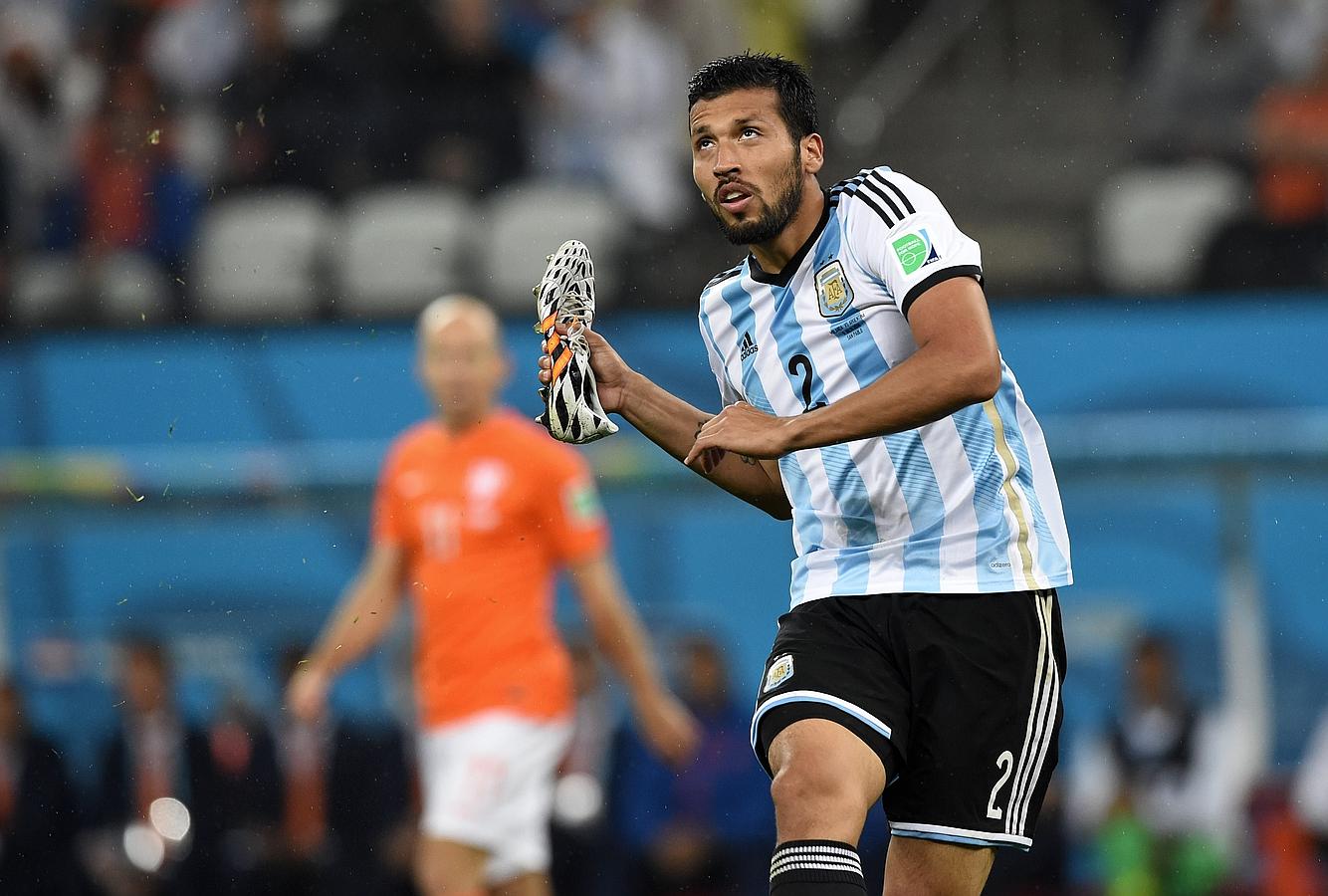 Garay, con una de sus zapatillas en la mano, despeja un balón.