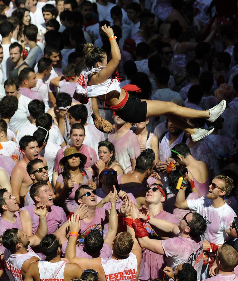 Jóvenes bañados en vino y con la indumentaria tradicional lanzan a una chica sobre el mar rojo y blanco de gente que celebra el chupinazo.