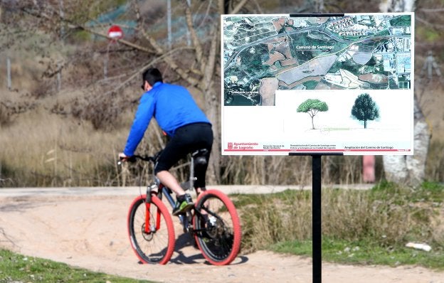 Un ciclista pasa junto a un cartel en el que se anuncian las obras previstas en La Grajera. :: JUAN MARín