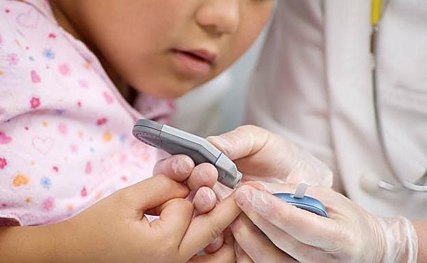 Un médico mide con un aparato la cantidad de azúcar en la sangre de un niño. 