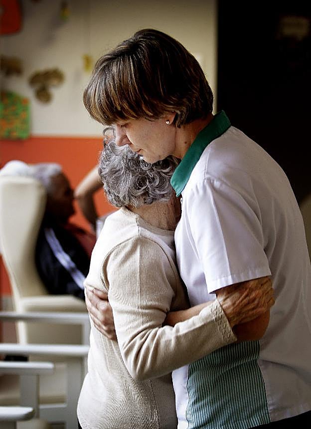 Una mujer sostiene a una paciente de alzhéimer en un centro de atención a las personas afectadas por esta enfermedad. 