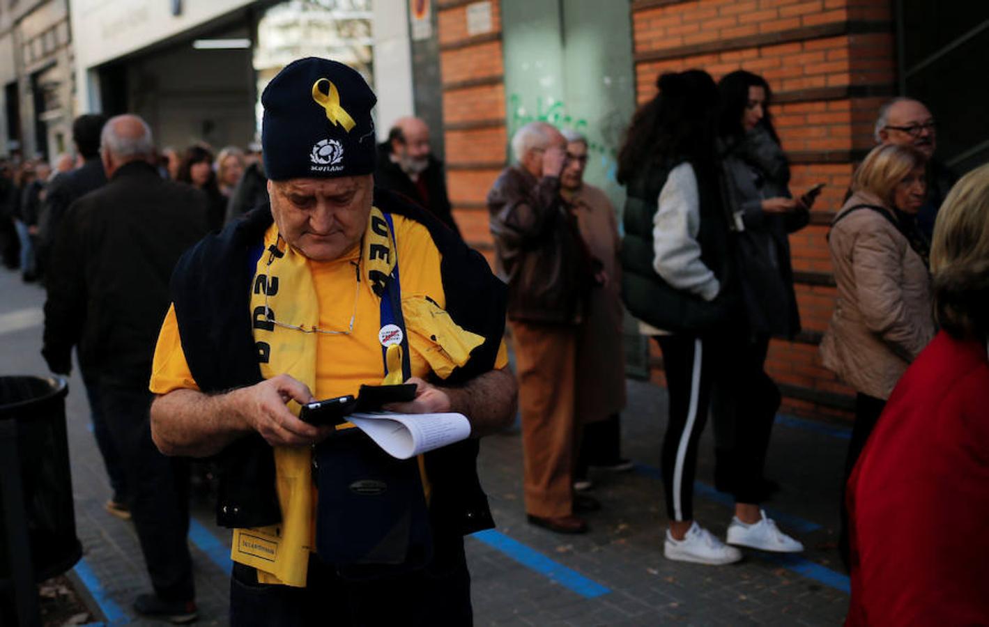 Un hombre que lleva una cinta amarilla en apoyo de los políticos catalanes encarcelados mira su teléfono después de votar. 