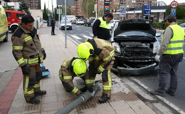 Destrozos en coche y farola con los bomberos trabajando en el lugar. 