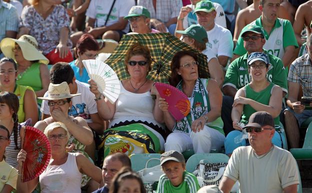 Aficionados del Betis se refrescan con abanicos ante las altas temperaturas.