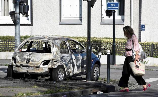 Una mujer pasea junto a un coche quemado en el barrio de Breil de Nantes.