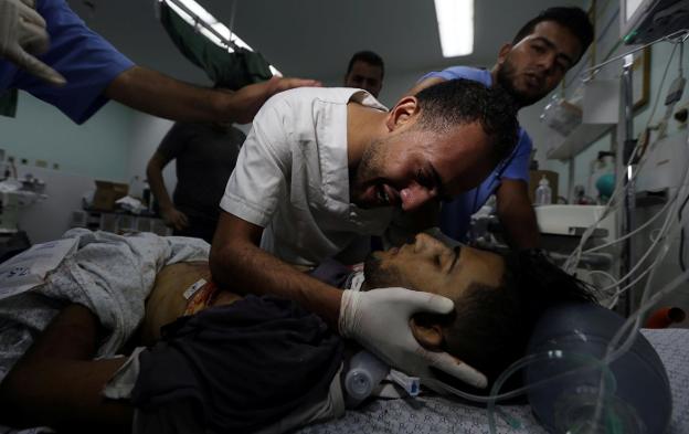 Un amigo del sanitario palestino fallecido ayer en Gaza por disparos de francotiradores israelíes llora junto a su cuerpo. :: reuters