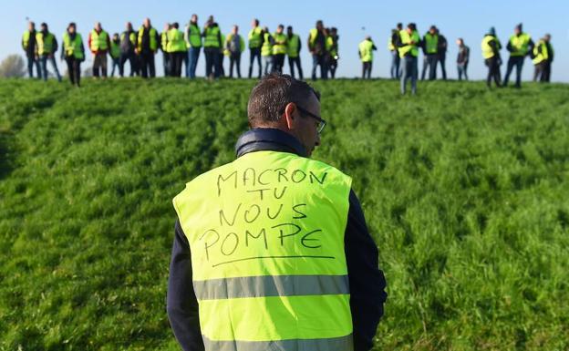Un hombre usa un chaleco amarillo que dice «Macron nos bombea».