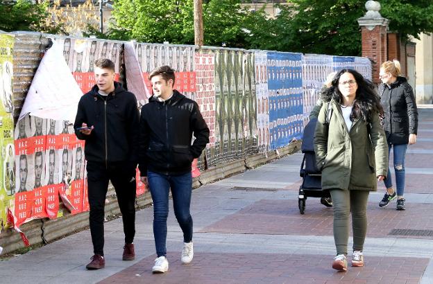 Paseantes en Logroño, delante de una pared decorada con carteles electorales. 