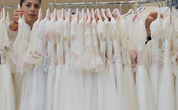 Perchas con un amplio abanico de vestidos de comunión para niñas, desde los modelos más clásicos a otros más modernos, y, arriba, crucifijo en unas manos infantiles.