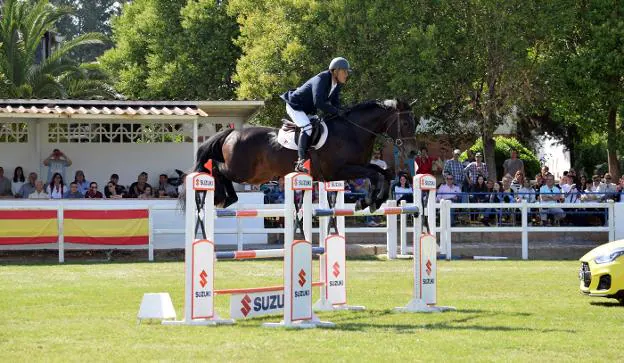 El público mira con admiración como jinete y caballo superan un salto. :