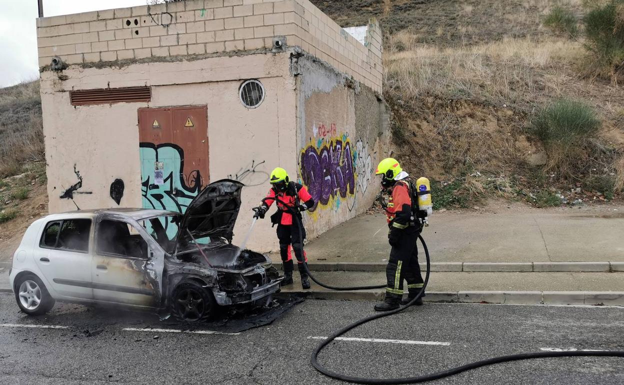 Los bomberos sofocan el fuego, junto al coche afectado.