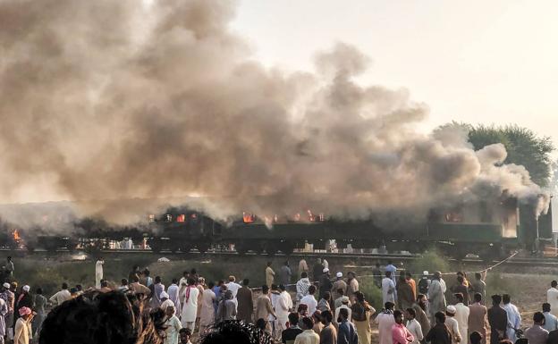 Decenas de pakistaníes se concentran junto a los vagones del tren quemado cerca de Rahim Yar Khan en Punjab (Pakistán).