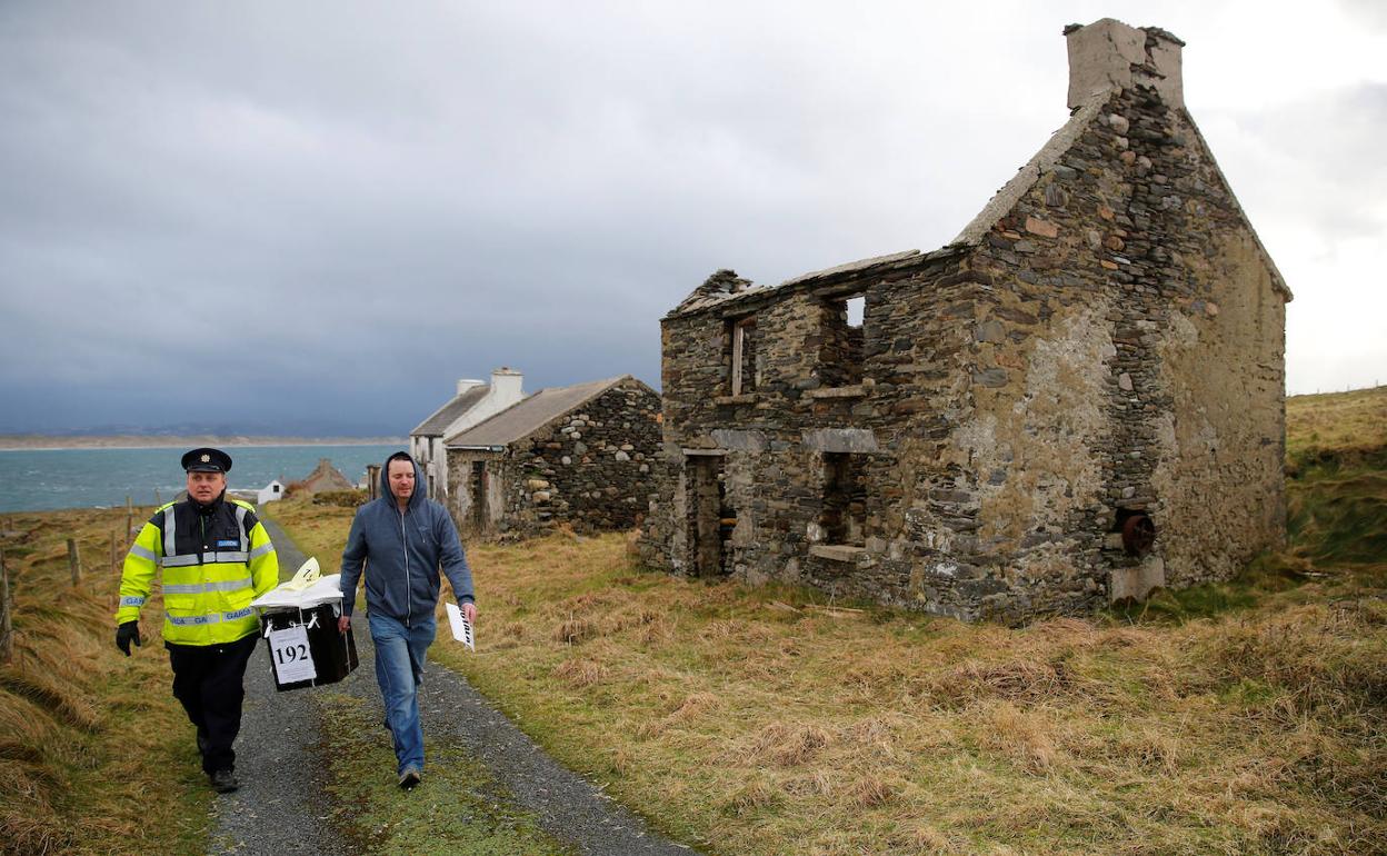 Un guardia y un responsable las elecciones transportan una urna para los comicios en la isla Inishbofin, en Irlanda.