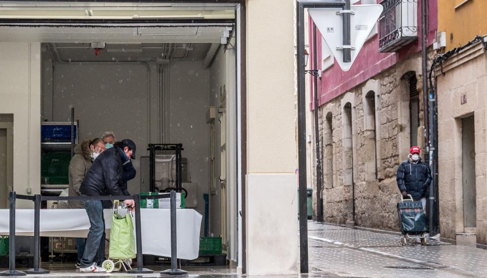 Un hombre introduce en el carro de la compra su comida del día, en la zona de almacén de la Cocina Económica en la calle Cadena, donde espera otro usuario. 