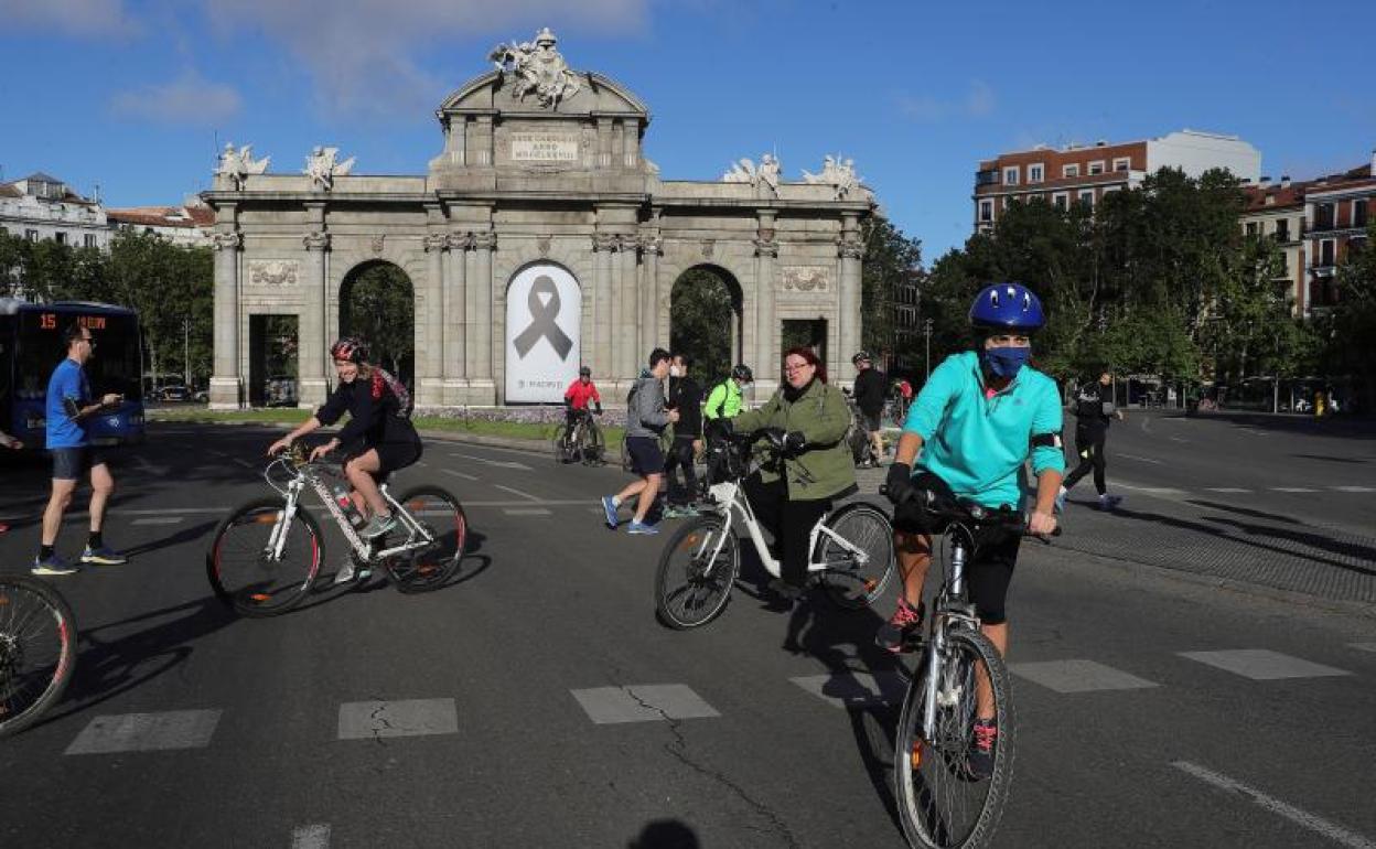 Varias personas y ciclistas en las inmediaciones de la Puerta de Alcalá (Madrid). 