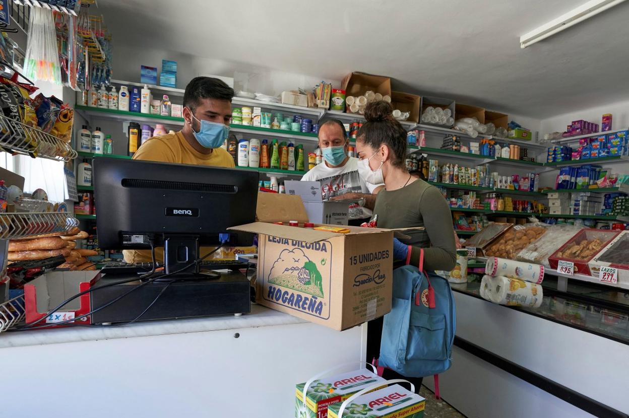 Unos clientes con mascarilla comprando en una tienda. 