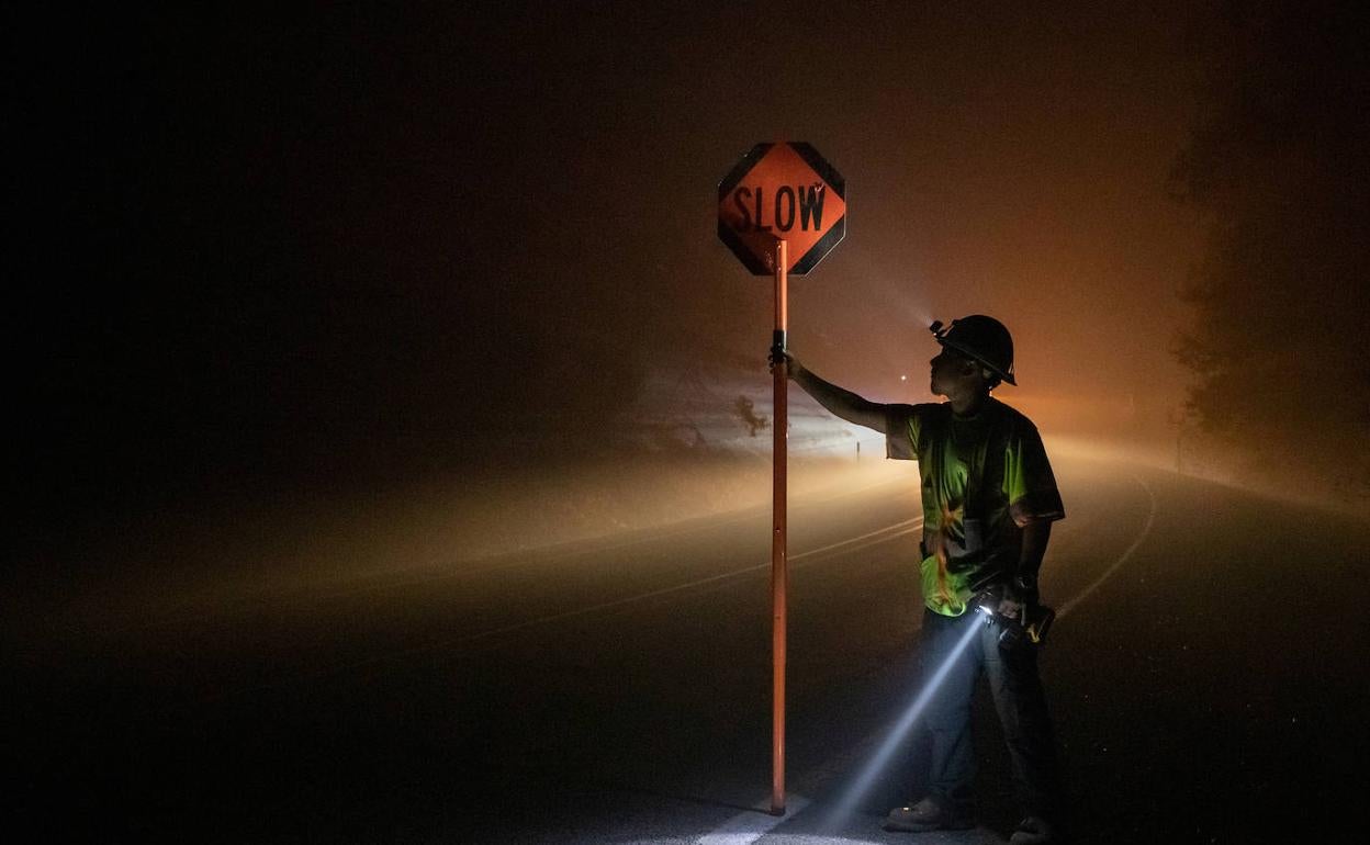 Un bombero sujeta un cartel pidiendo circular despacio por el humo de los incendios forestales en una carretera de Oregón.