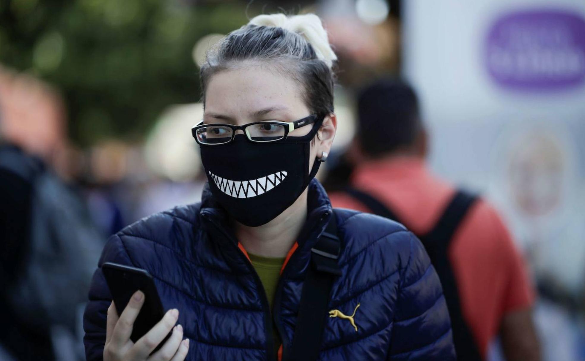 Conexión y riesgo. Una mujer con mascarilla mientras revisa su teléfono móvil.