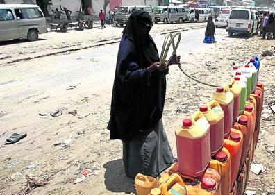 Imagen secundaria 1 - Policías festejan encaramados a un tanque de petróleo un rescate marítimo. Abajo, una vendedera callejera de gasolina en Mogadishu y una mujer de de beber a un nño desnutrido.