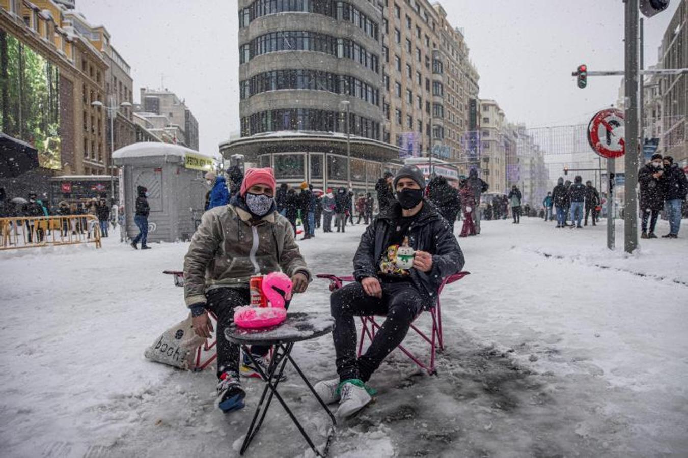 Dos personas sentadas en una improvisada terraza, posan en la madrileña Plaza de Callao con la Gran Vía de Madrid, tras el paso de la borrasca Filomena