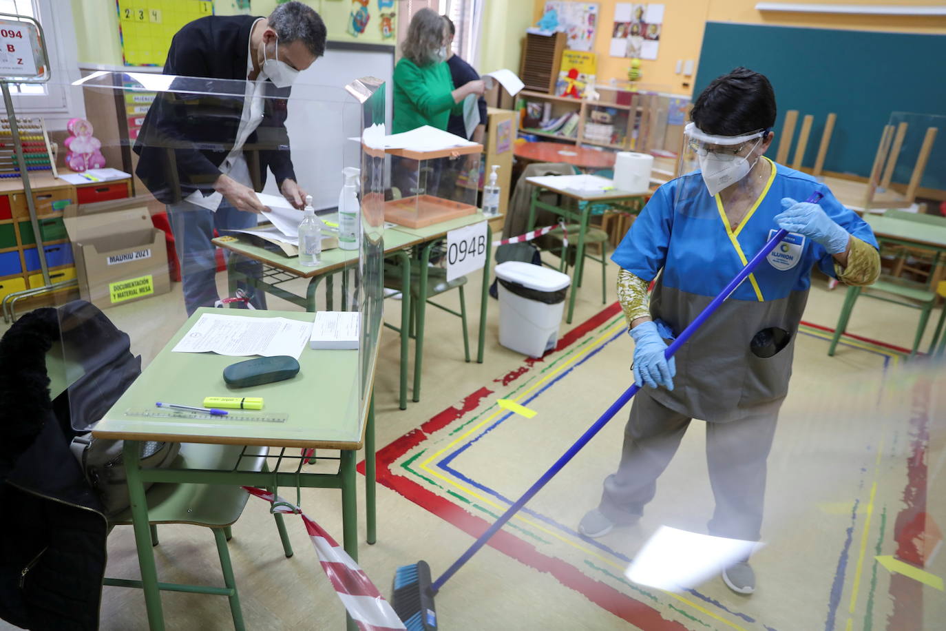 Una trabajadora vestido con equipo de protección barre el suelo de un colegio electoral antes del inicio de las elecciones regionales de Madrid.