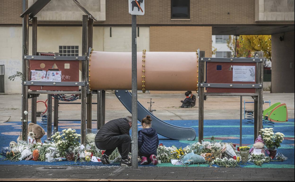 Un hombre y una niña depositan flores en la zona de juegos del parque del que el presunto asesino se llevó con engaños a Álex.