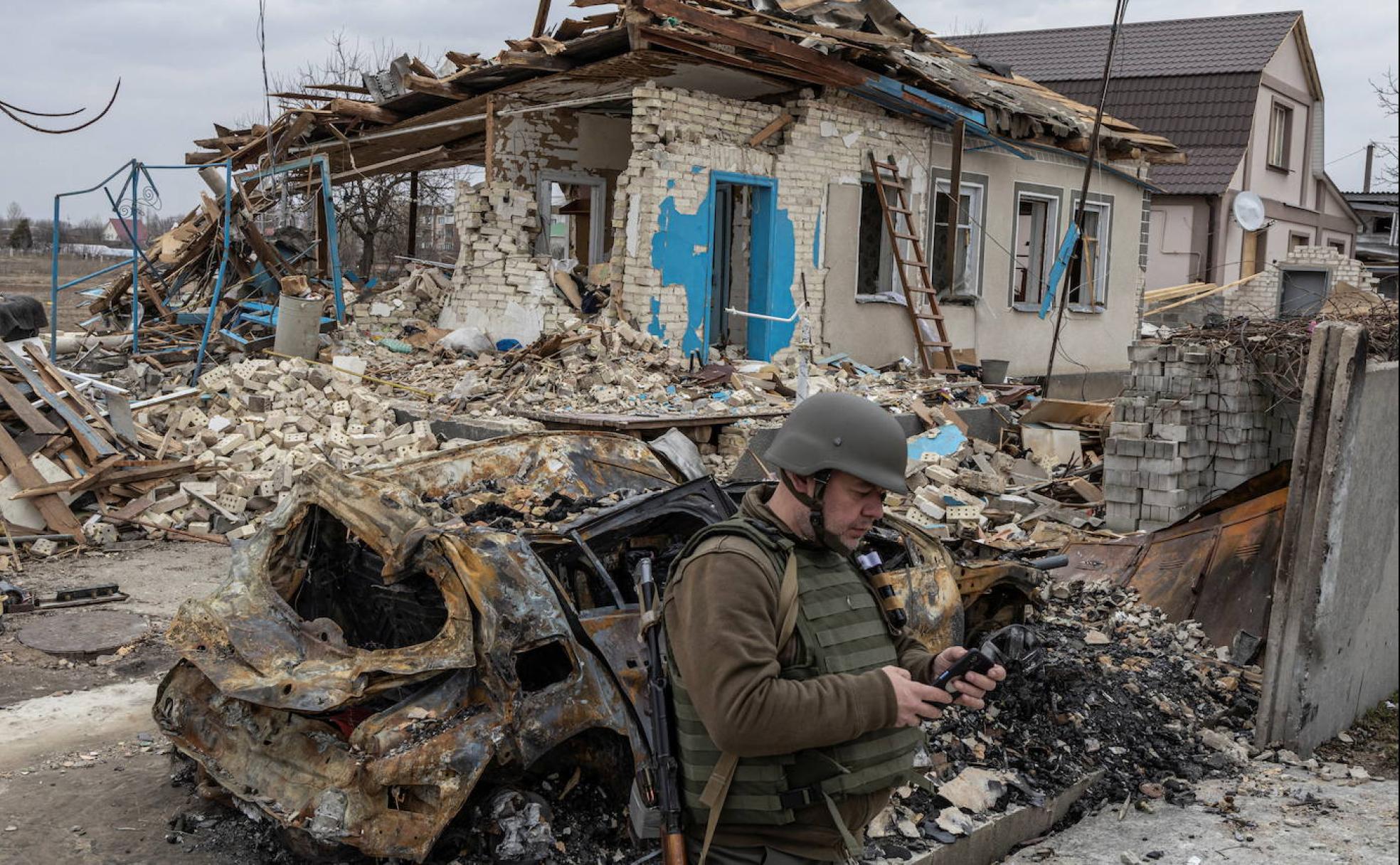 Un soldado ucraniano mira su móvil ante los destrozos provocados por los bombardeos rusos. 