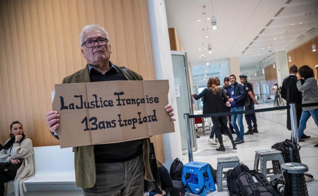 Winfried Schmidt, familiar de unas de las víctimas, a la entrada de los juzgados con un cartel que reza 'La Justicia francesa 13 años demasiado tarde', este lunes en París.