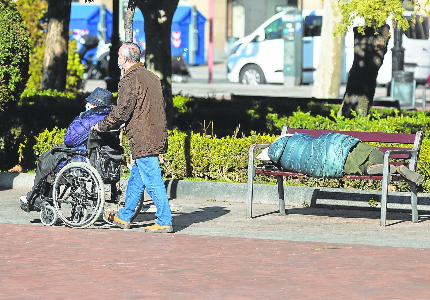 Una persona duerme en un banco del Espolón a plena luz del día, mientras algunos ciudadanos pasean por el céntrico parque logroñés. 