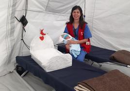 Carmen sostiene en brazos a uno de los bebés nacidos en el hospital de la Aecid, junto a una cuna fabricada allí para los recién nacidos.