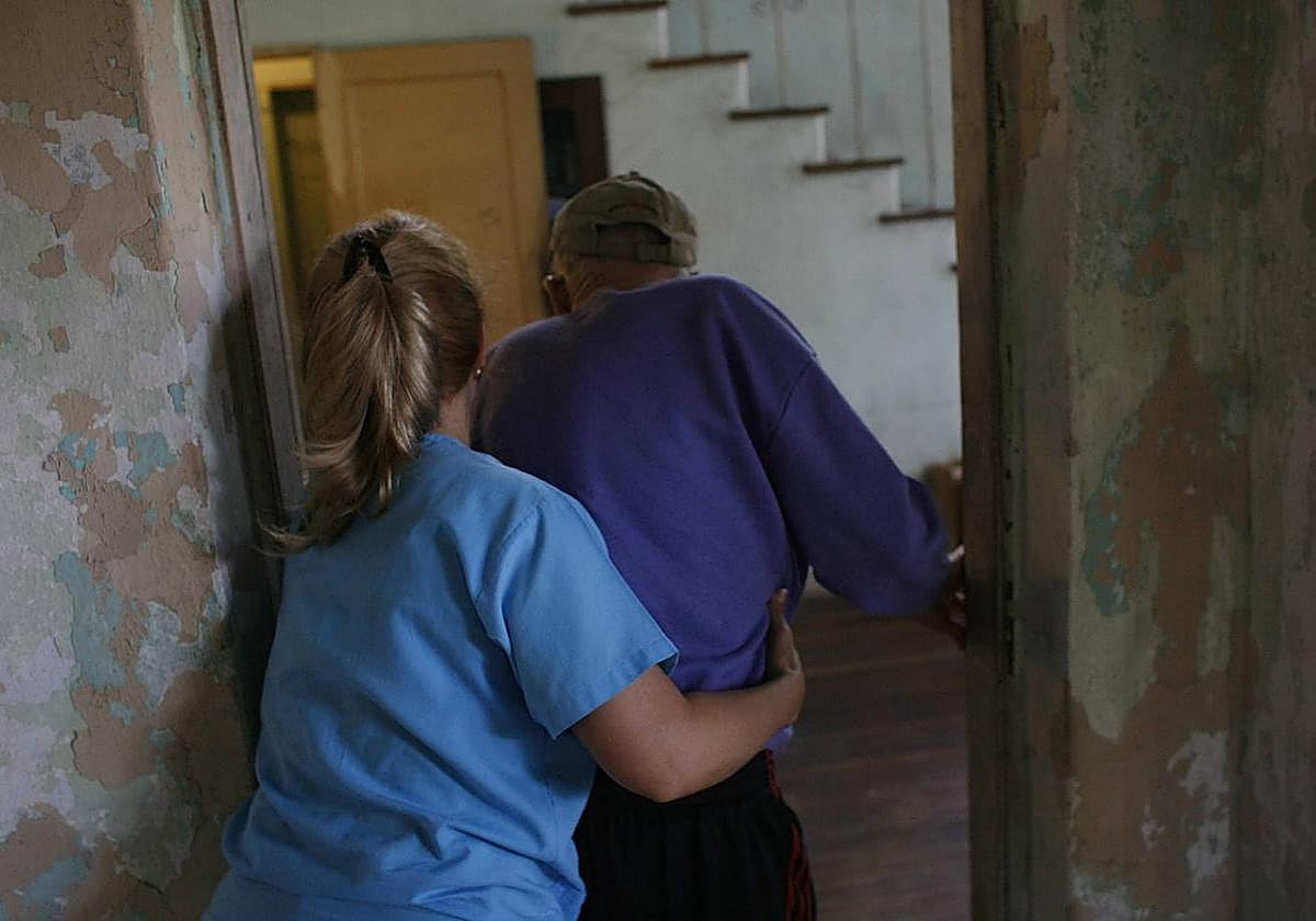 Un anciano es ayudado a desplazarse por una enfermera.