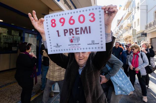 Uno de los propietarios de la administración número 1 de L'Escala (Girona) posa con el número agraciado con el primer premio de la Lotería de El Niño.