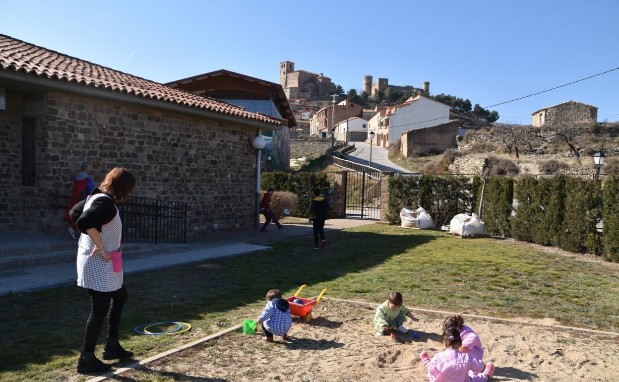 Los niños del colegio de Cornago disfrutan en el arenero del patio, con el castillo y la iglesia de fondo. 